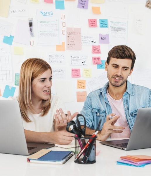 smiling-male-female-sitting-desk-talking-looking-laptop